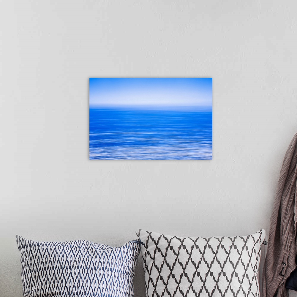 A bohemian room featuring Silky calm blue open sea [ocean] with fog or mist over water. Blue sky.