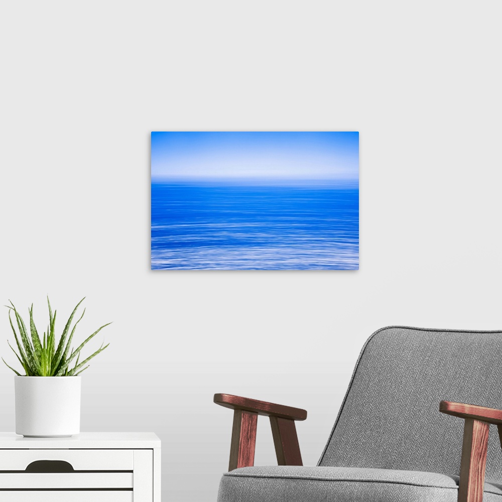 A modern room featuring Silky calm blue open sea [ocean] with fog or mist over water. Blue sky.
