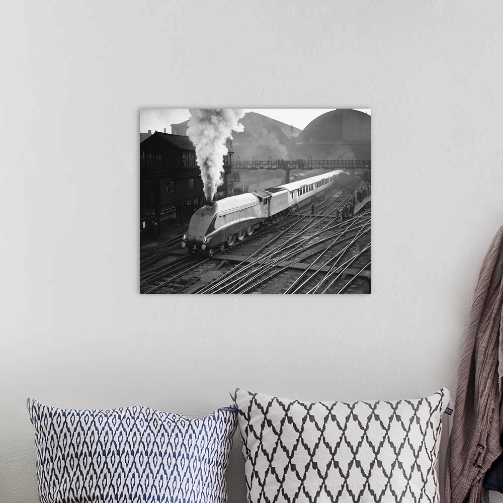 A bohemian room featuring The gleaming Silver Link emits a jet of steam as it passes a platform crowded with onlookers.