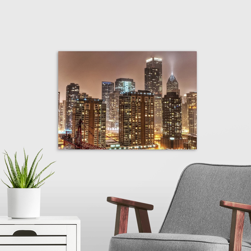 A modern room featuring A photograph taken of the Chicago skyline at night with the buildings illuminated and snow beginn...