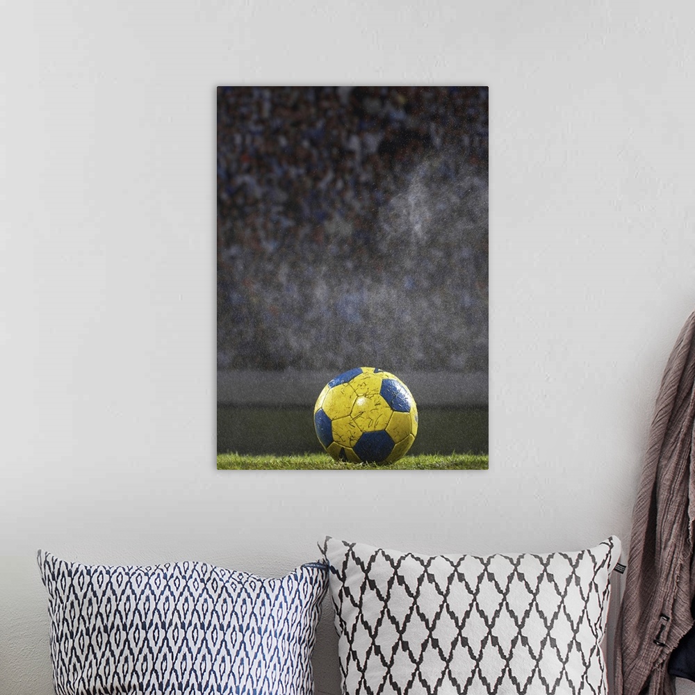 A bohemian room featuring A soccer ball that is covered with wet grass is photographed sitting on a field with the crowd ou...