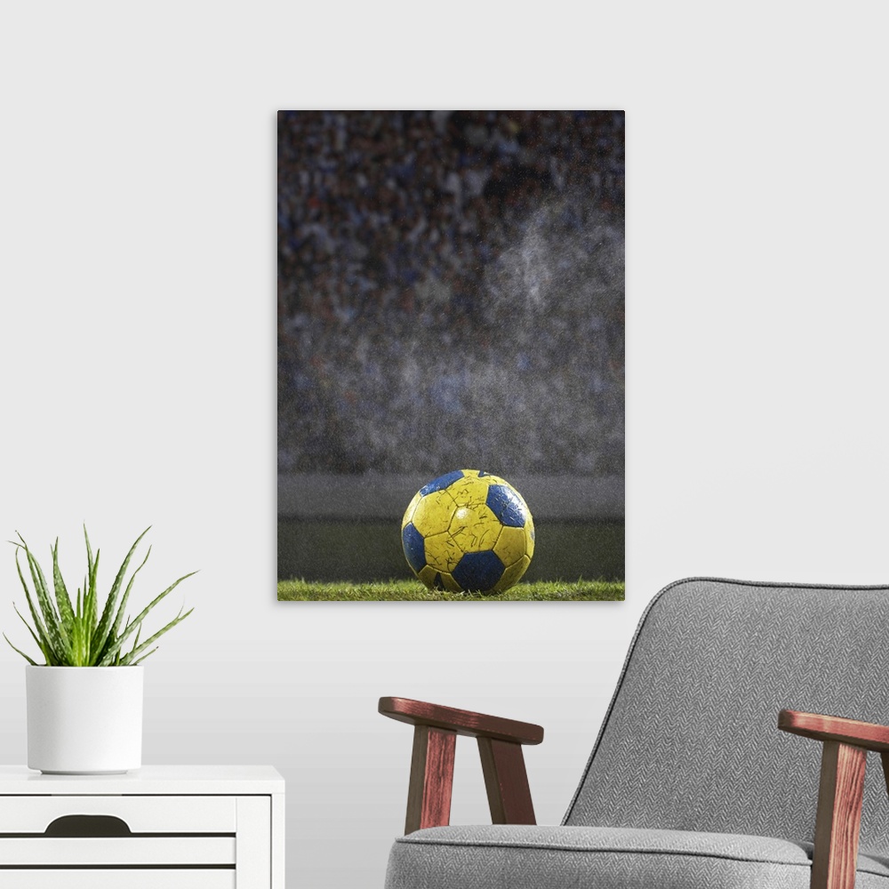 A modern room featuring A soccer ball that is covered with wet grass is photographed sitting on a field with the crowd ou...