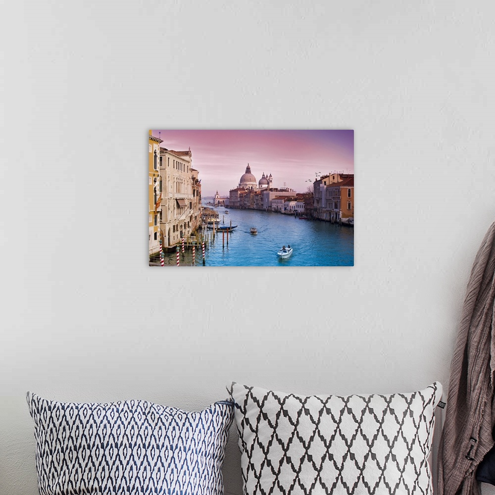 A bohemian room featuring Wall art of buildings on either side of an Italian canal with boats floating through the water.