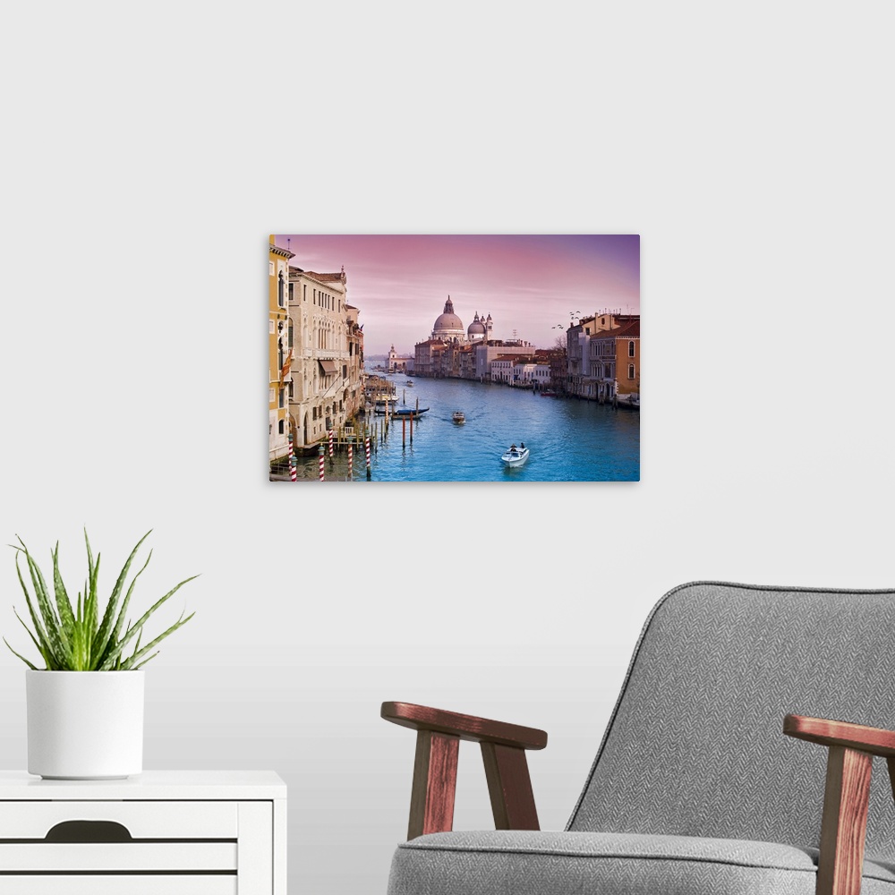 A modern room featuring Wall art of buildings on either side of an Italian canal with boats floating through the water.
