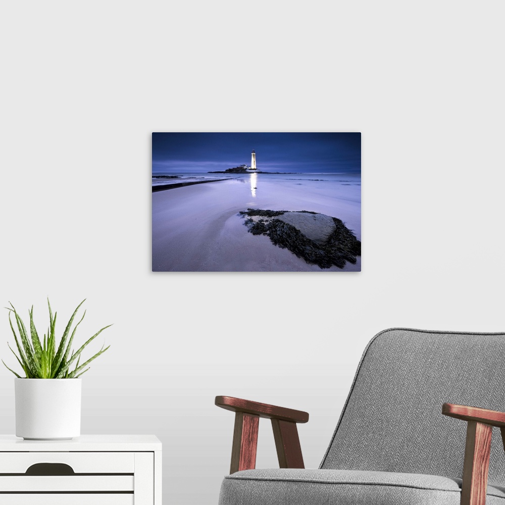 A modern room featuring St.Marys Lighthouse, Whitley Bay, glowing at night in blue hour, reflected on sand in front of se...