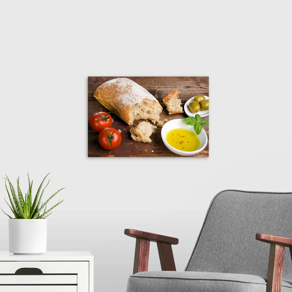 A modern room featuring Big photograph focuses on a loaf of crusty bread sitting on a wooden table alongside a couple gro...