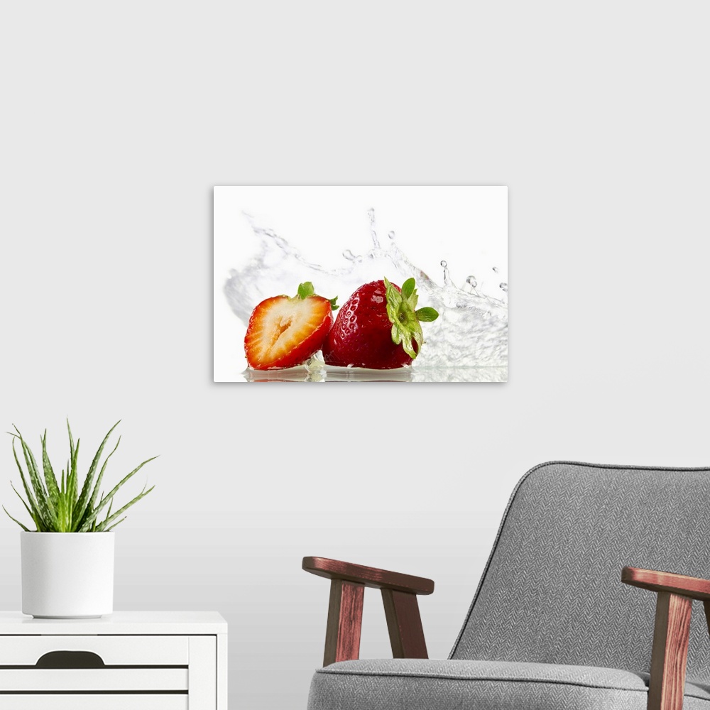 A modern room featuring Horizontal, photograph on large canvas of two strawberries, one cut in half, with water splashing...