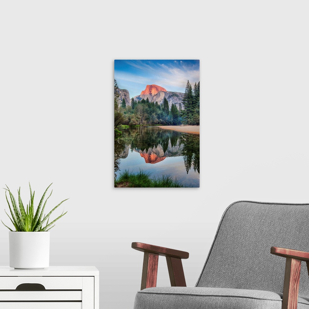 A modern room featuring Half Dome in Yosemite National Park is reflected in the water of the Merced River at sunset.