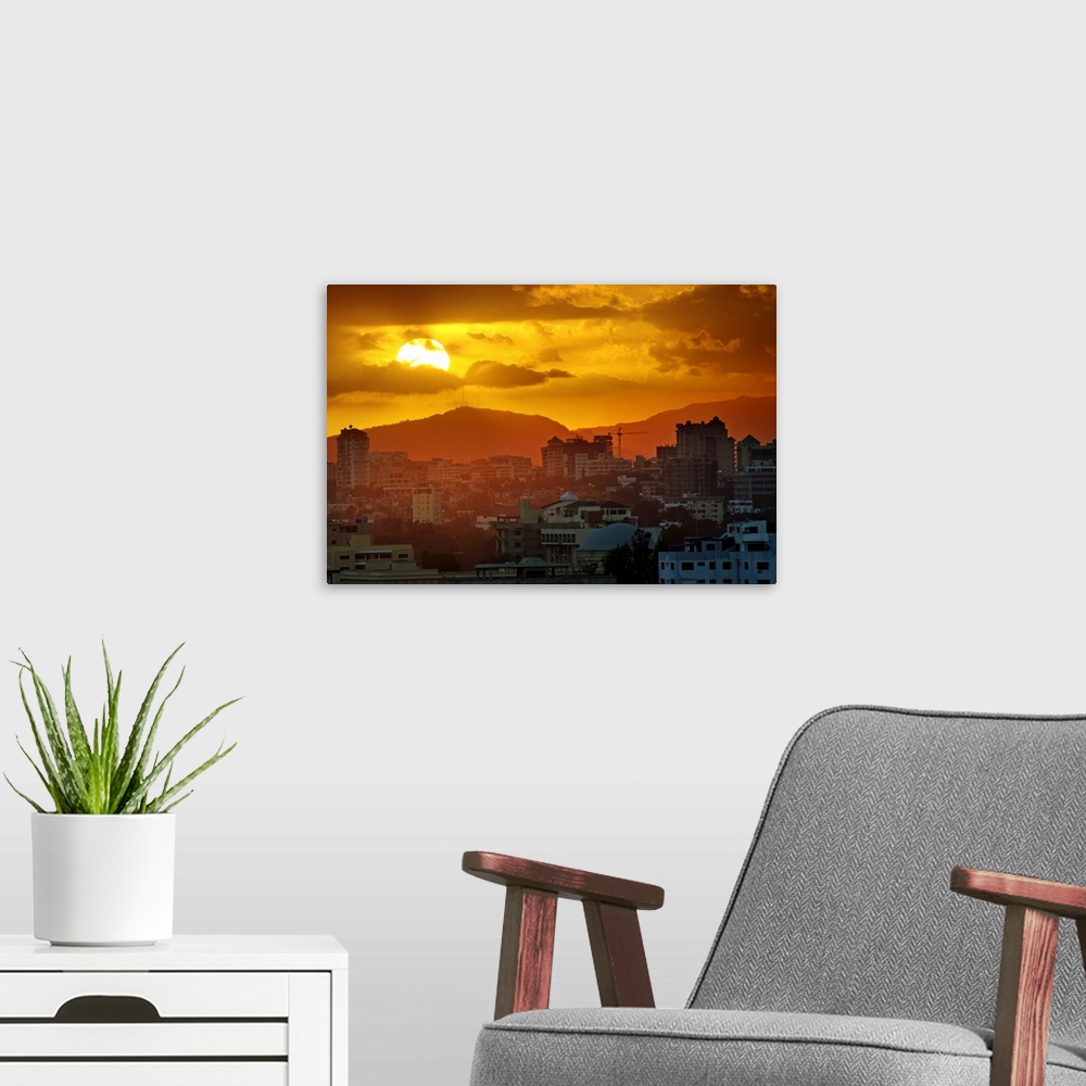 A modern room featuring Sunset, Santo Domingo, Domenican Republic, large sun, cloudy sky, orange mood, mountains in backg...
