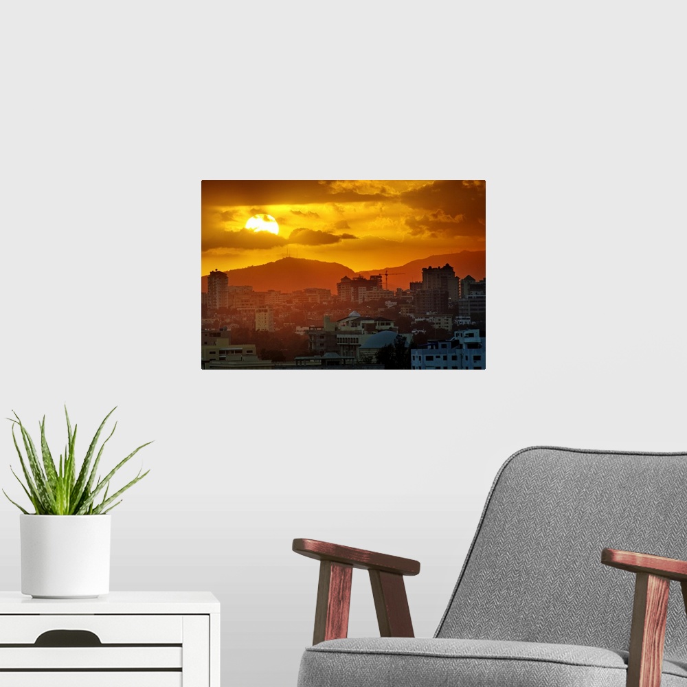 A modern room featuring Sunset, Santo Domingo, Domenican Republic, large sun, cloudy sky, orange mood, mountains in backg...