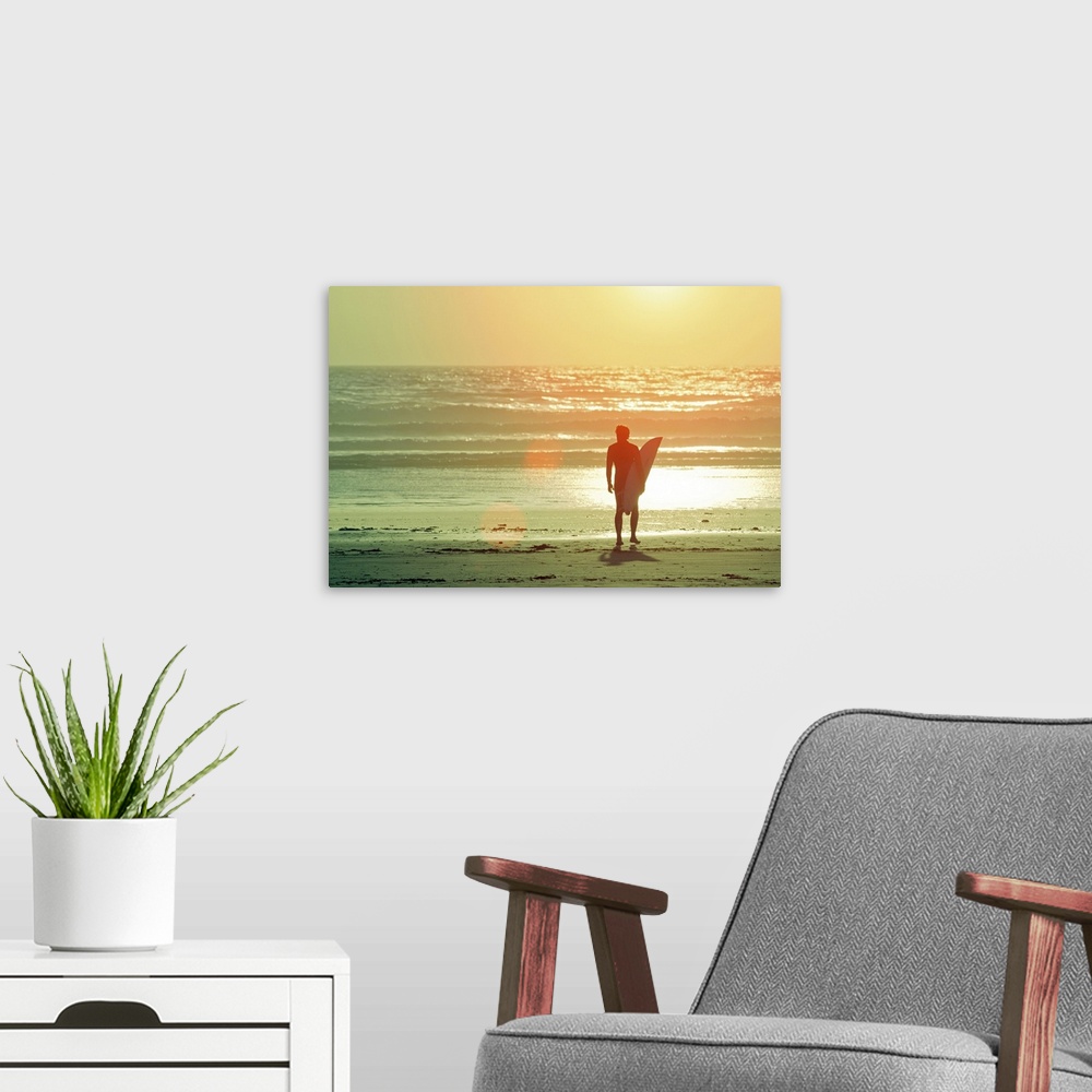 A modern room featuring Big print on canvas of a surfer with a surfboard silhouetted against the setting sun looking out ...