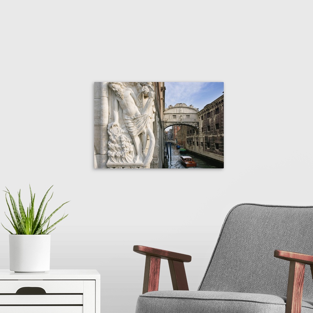 A modern room featuring Large photograph taken of a bridge in Italy with a boat floating under it and a statue of a man i...