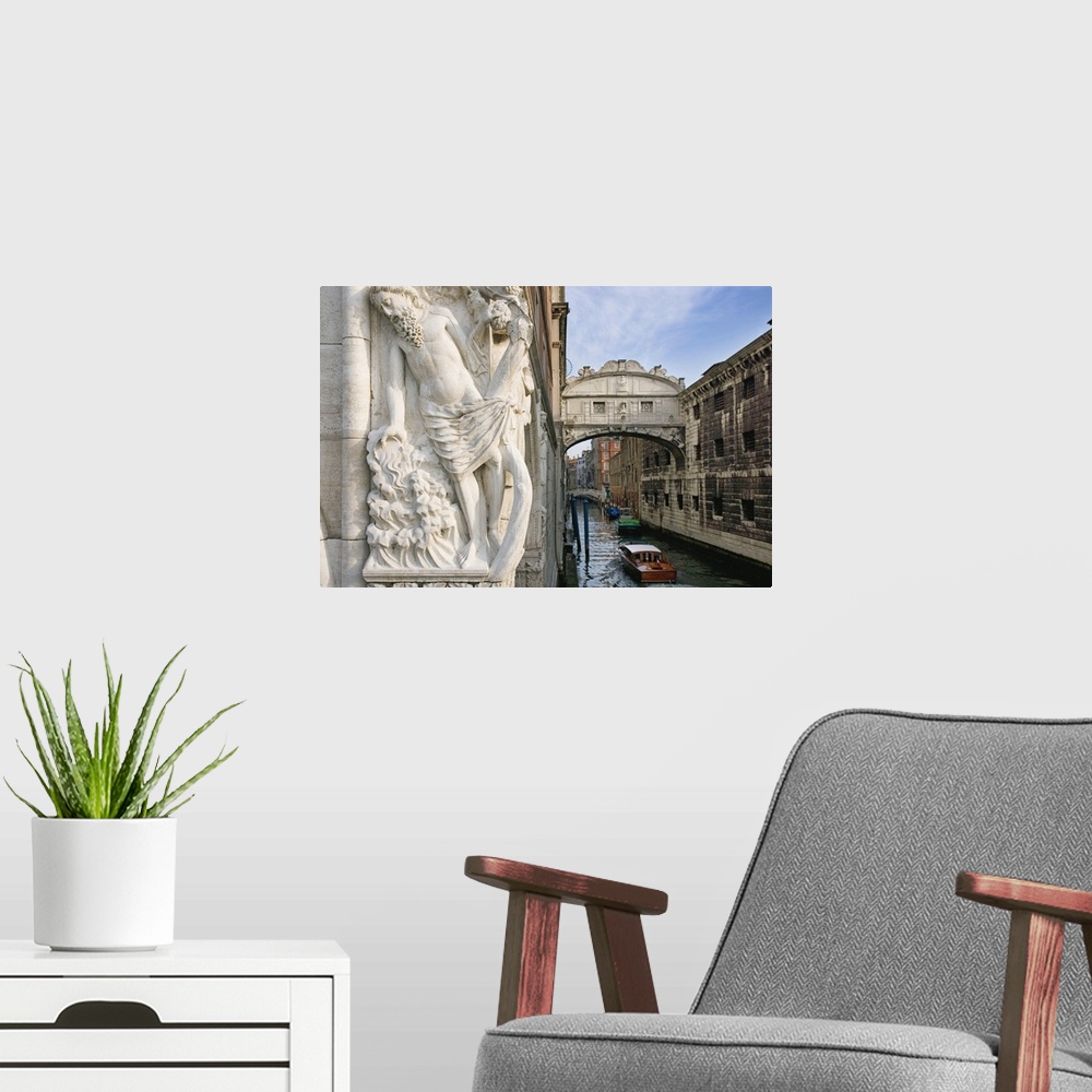 A modern room featuring Large photograph taken of a bridge in Italy with a boat floating under it and a statue of a man i...