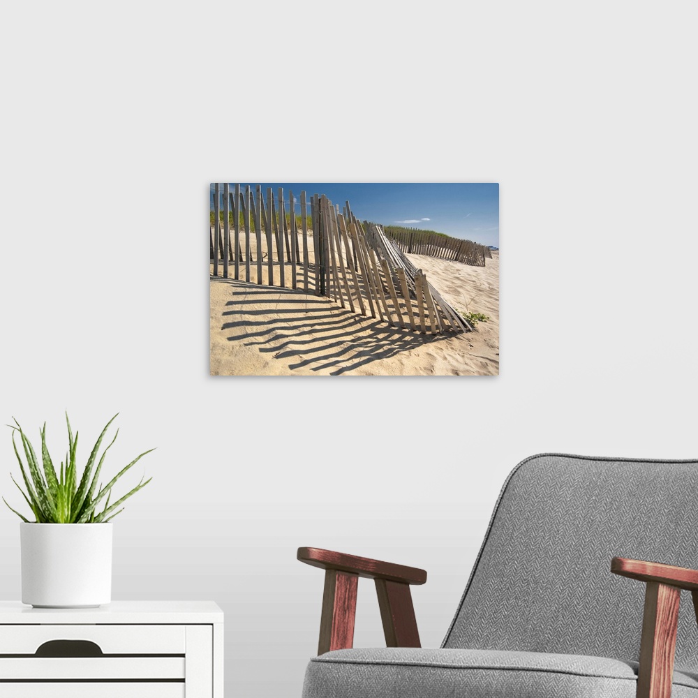A modern room featuring The low sun casts long shadows of a wooden fence on a sandy dune by the ocean.