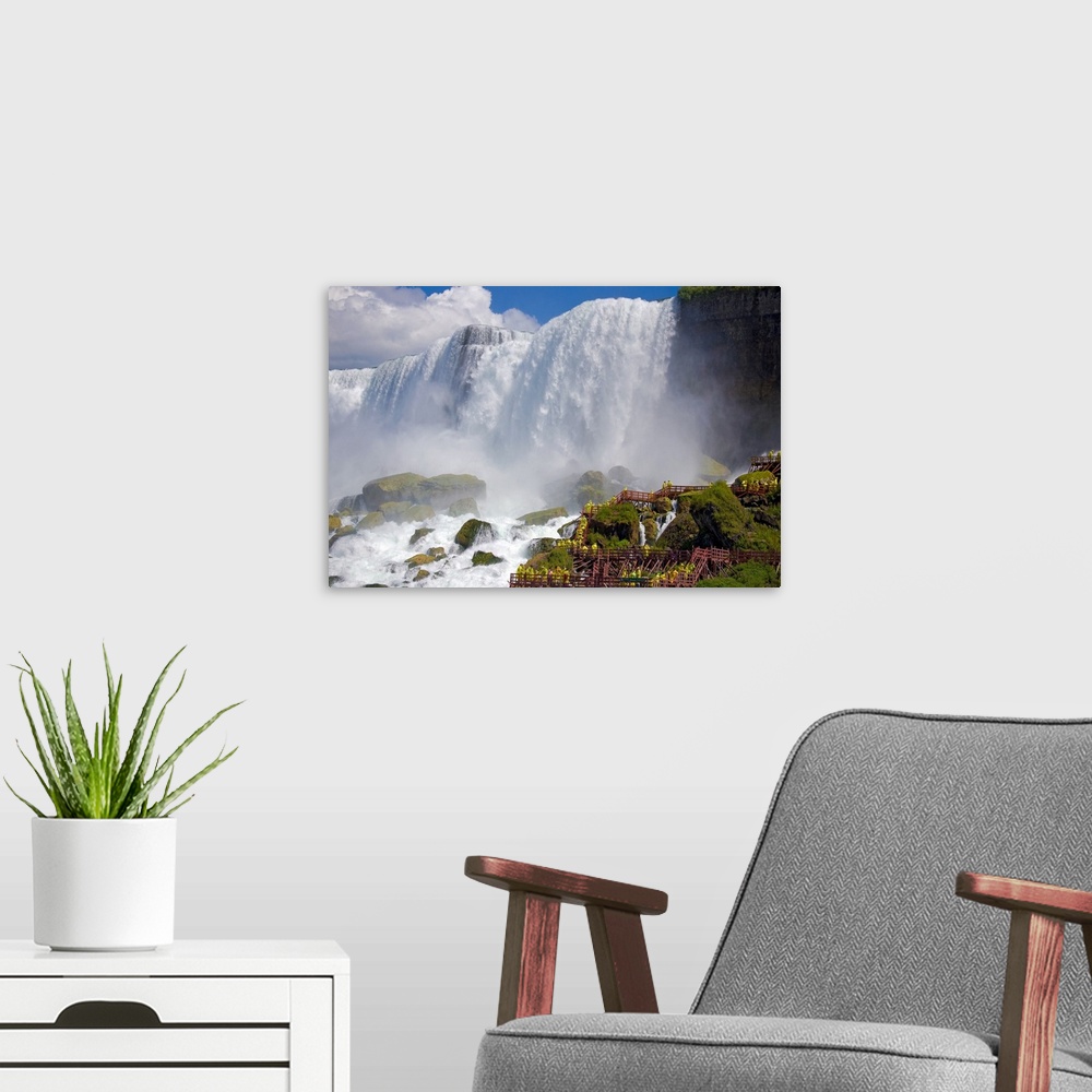 A modern room featuring The immense Niagara falls are photographed from below showing the large rocks at the bottom that ...