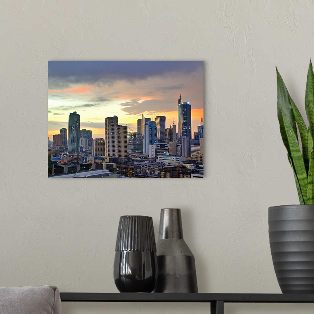 A modern room featuring The sun setting light up low clouds over the Makati City, Manila Skyline. Many Tall buildings and...