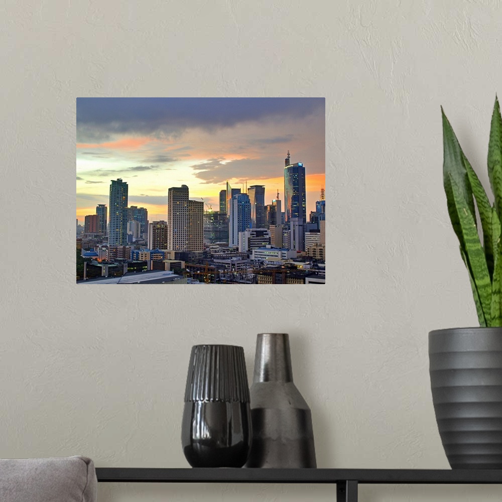 A modern room featuring The sun setting light up low clouds over the Makati City, Manila Skyline. Many Tall buildings and...