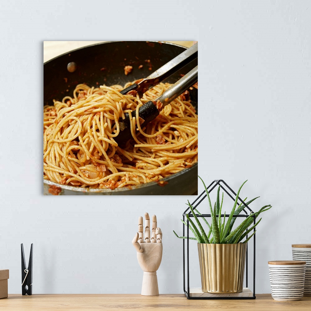A bohemian room featuring Tongs tossing spaghetti with meat sauce in pan