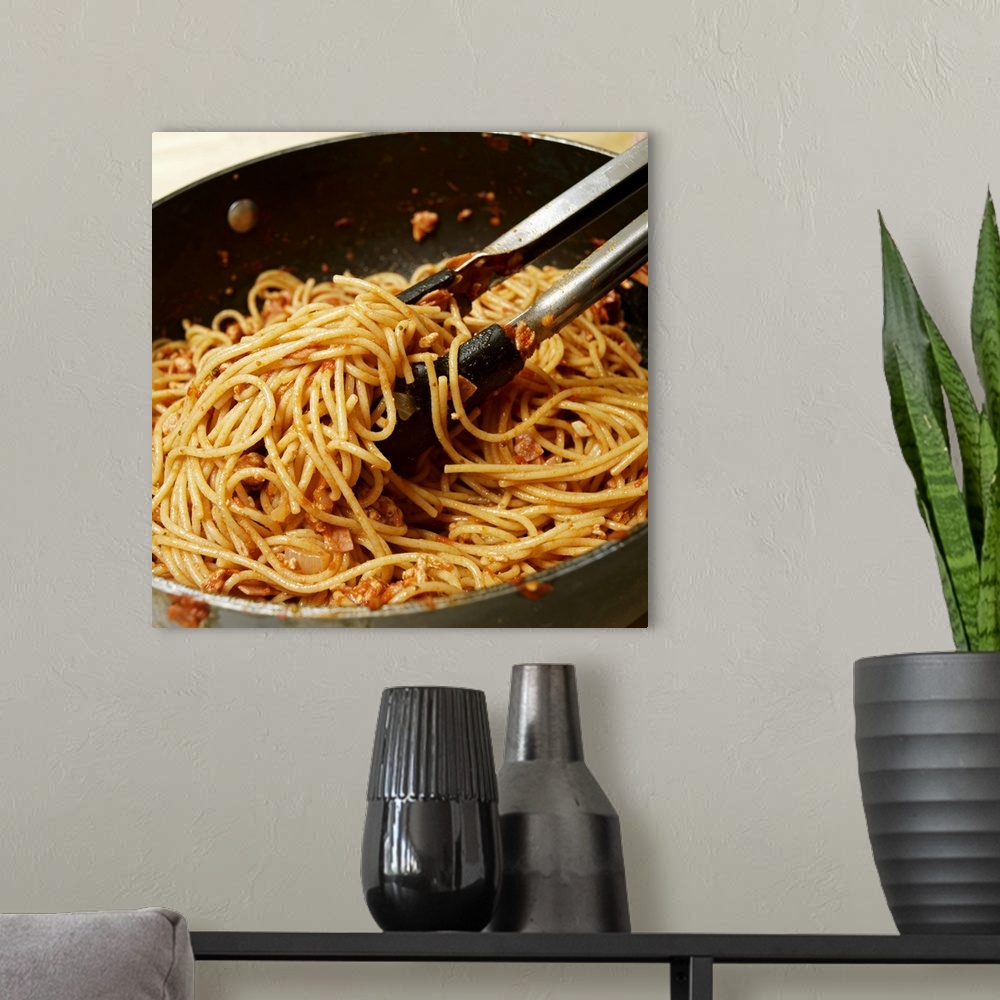 A modern room featuring Tongs tossing spaghetti with meat sauce in pan