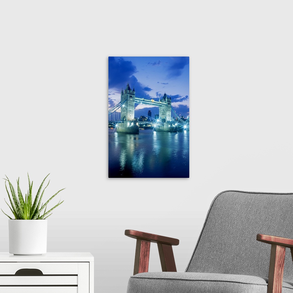 A modern room featuring Vertical photograph on a large wall hanging of the Tower Bridge, lit up at night, the London skyl...