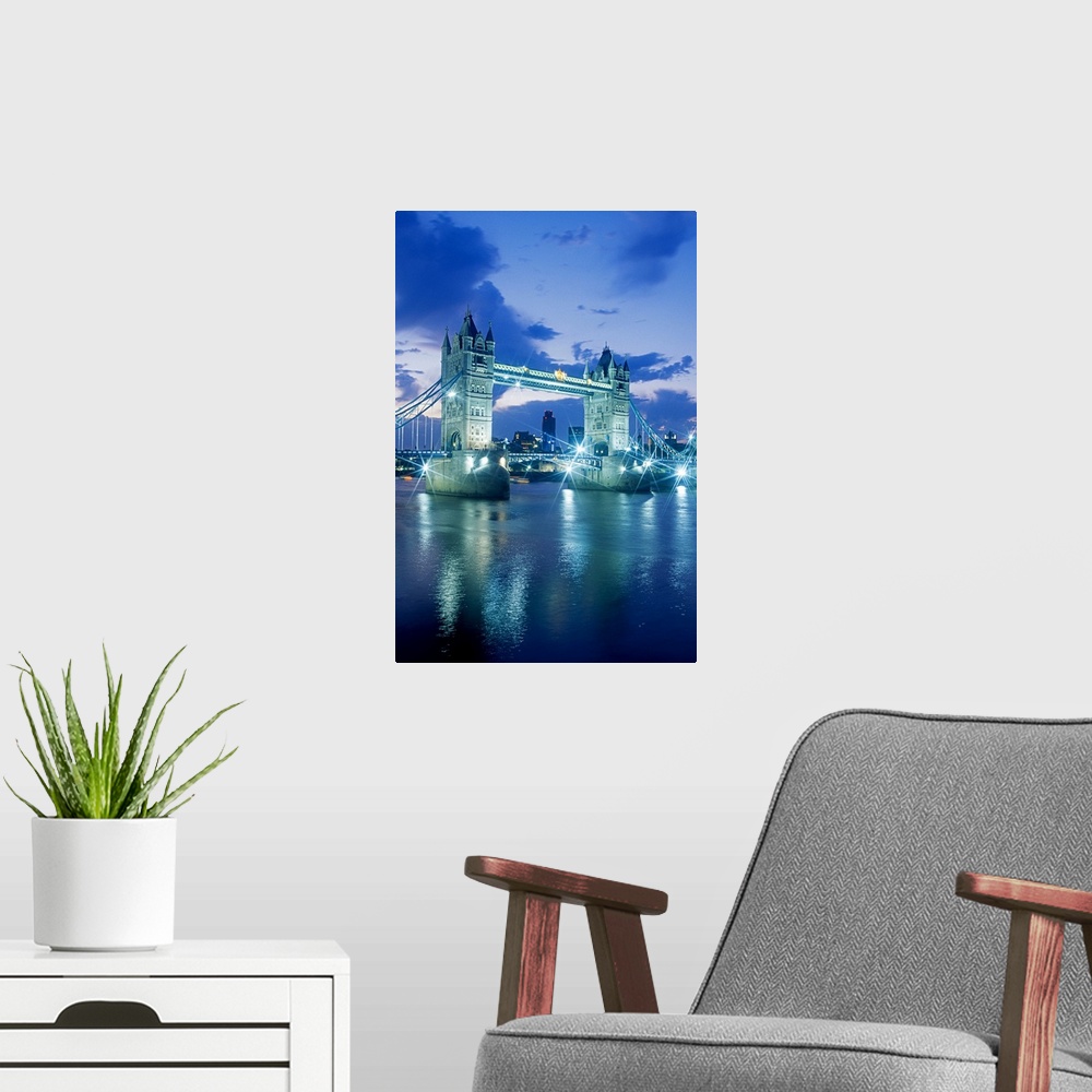 A modern room featuring Vertical photograph on a large wall hanging of the Tower Bridge, lit up at night, the London skyl...