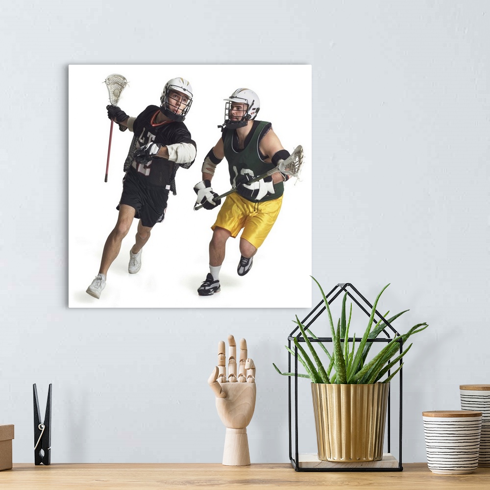A bohemian room featuring two caucasian male lacrosse players from opposite teams run as the one in the green jersey tries ...