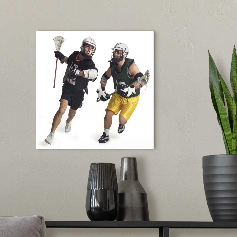 A modern room featuring two caucasian male lacrosse players from opposite teams run as the one in the green jersey tries ...