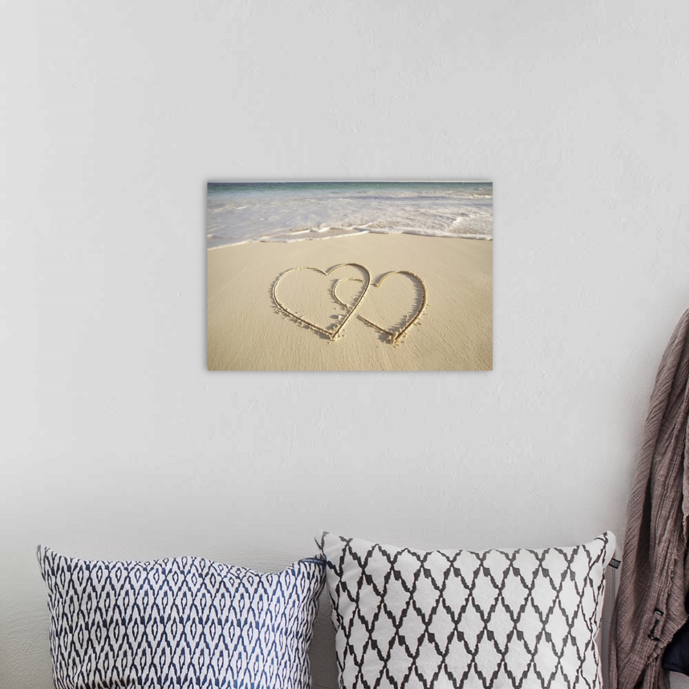 A bohemian room featuring Two overlying hearts drawn on the beach with incoming surf.