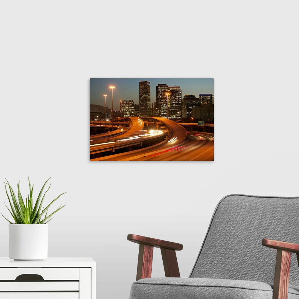 A modern room featuring Photograph of the Houston skyline taken at night with the buildings lit up and cars lights streak...