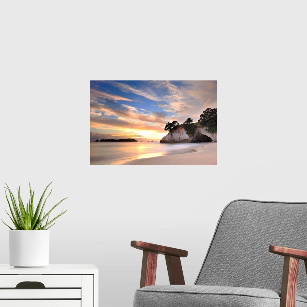 A modern room featuring Photograph of huge rock formation on beach under a cloudy sky.
