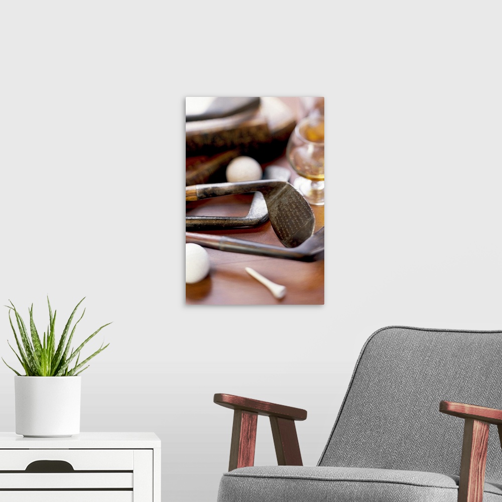 A modern room featuring Antique golf club heads are photographed laying on a table with golf balls, a tee and a glass of ...