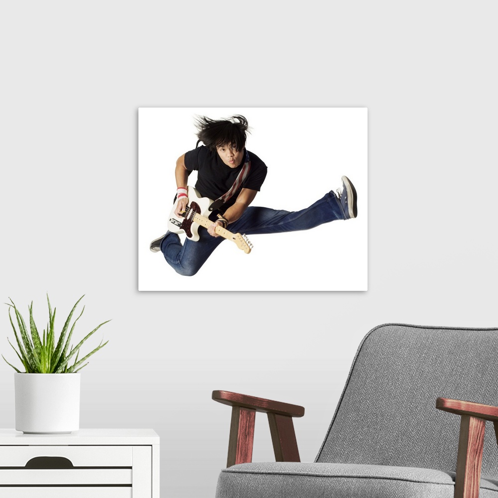 A modern room featuring an asian teenage male in jeans and a black shirt jumps up wildly with his electirc guitar