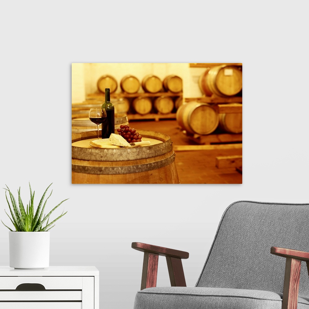 A modern room featuring A photograph in a wine cellar of an upright barrel with a glass of wine, grapes, and cheese sitti...