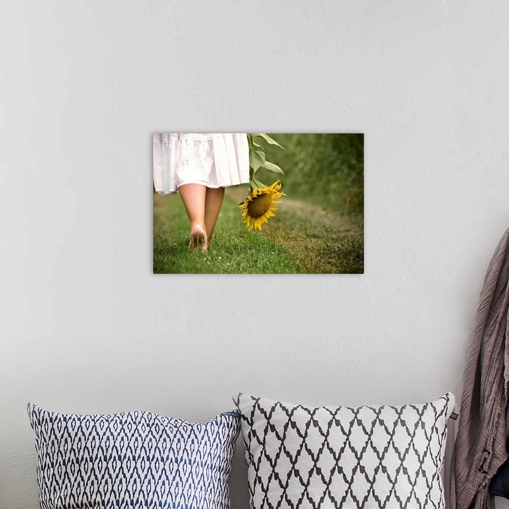 A bohemian room featuring Woman bare feet walking on grass holding sunflower.