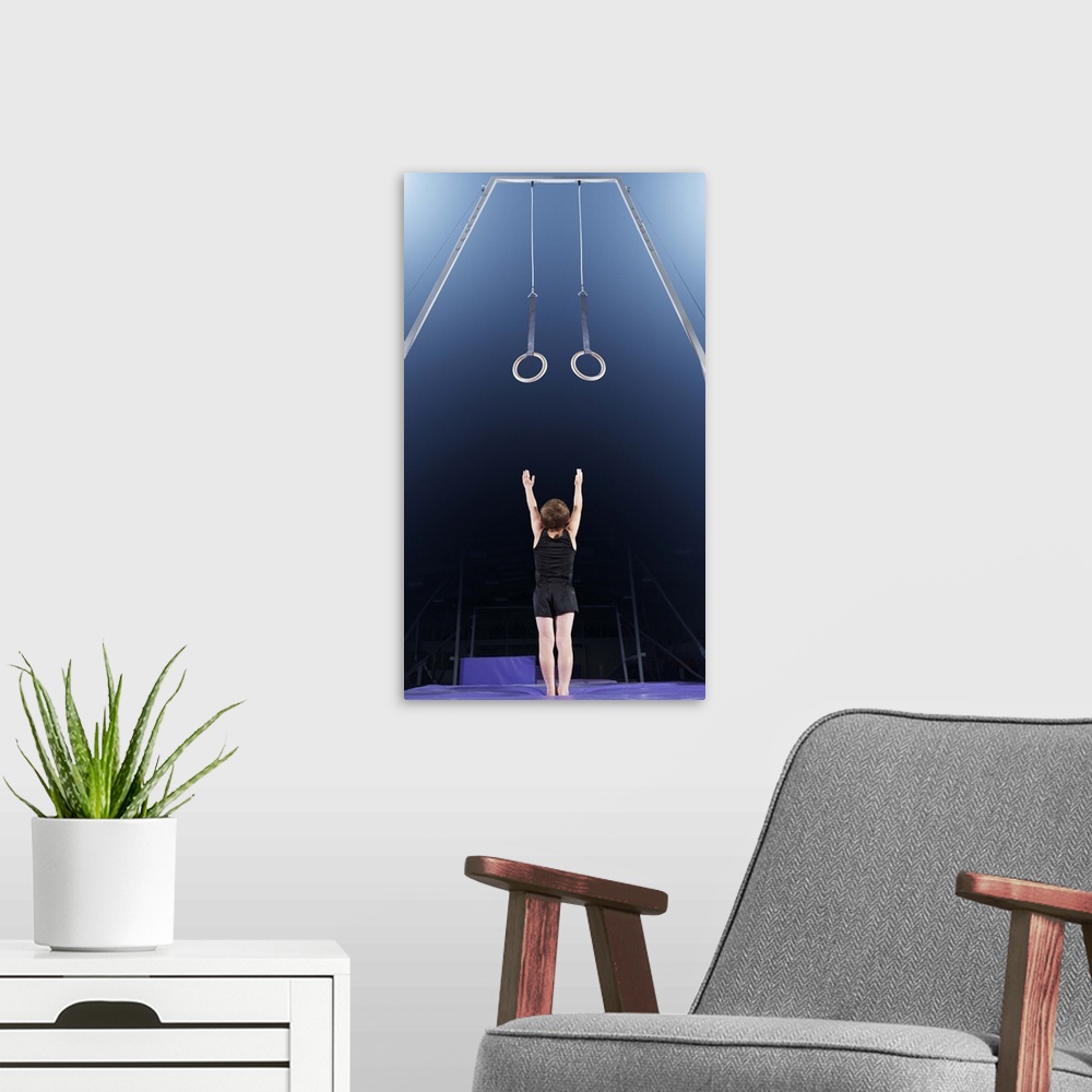 A modern room featuring Young male gymnast reaching up to rings