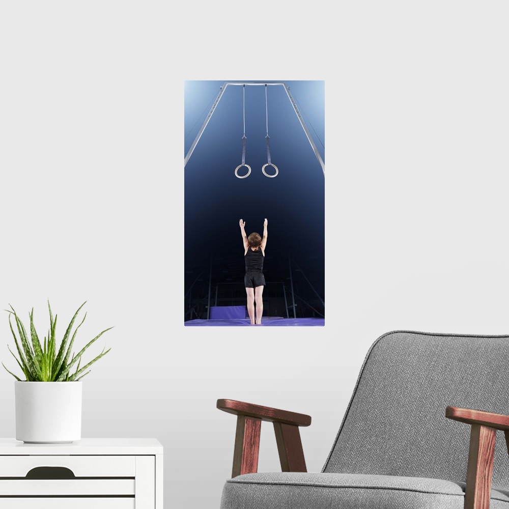 A modern room featuring Young male gymnast reaching up to rings