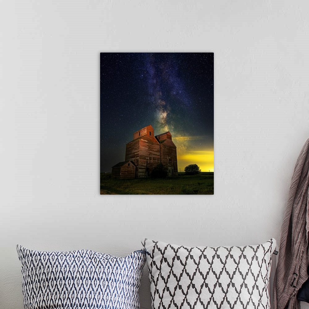A bohemian room featuring The Milky Way glows behind an old grain elevator in the ghost town of Arena, North Dakota.