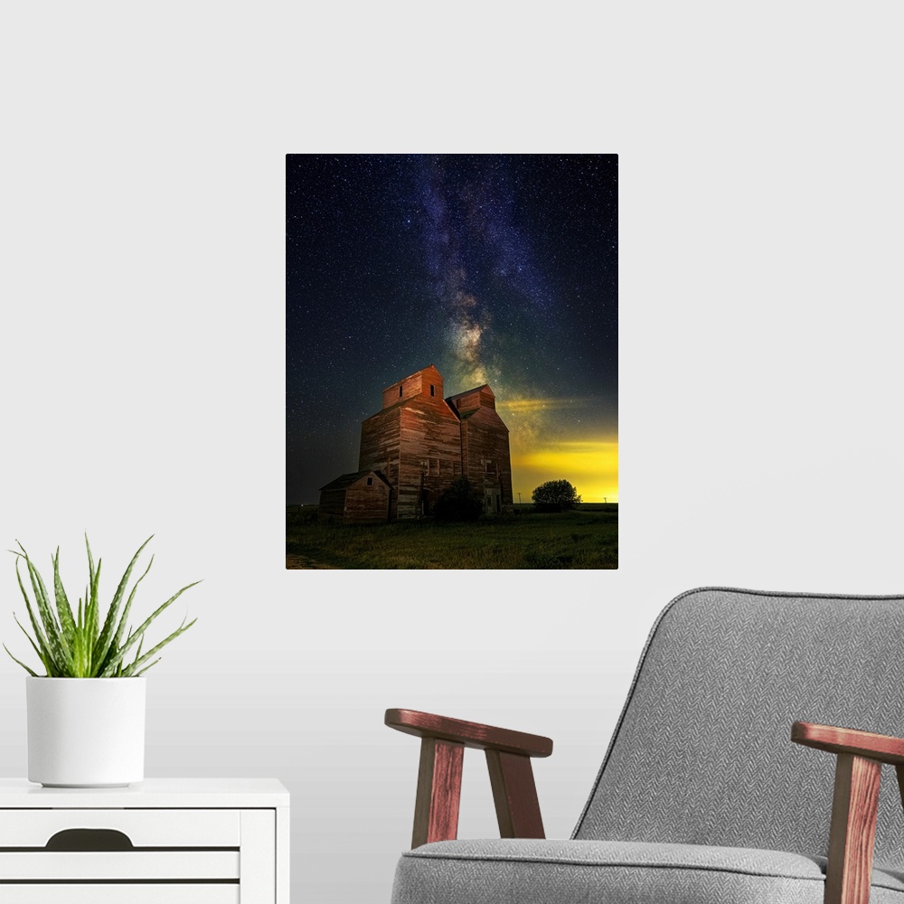 A modern room featuring The Milky Way glows behind an old grain elevator in the ghost town of Arena, North Dakota.