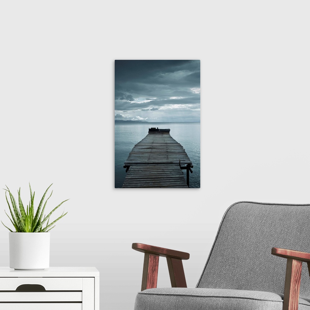 A modern room featuring Photograph of a weathered dock over calm water with dark clouds overhead.