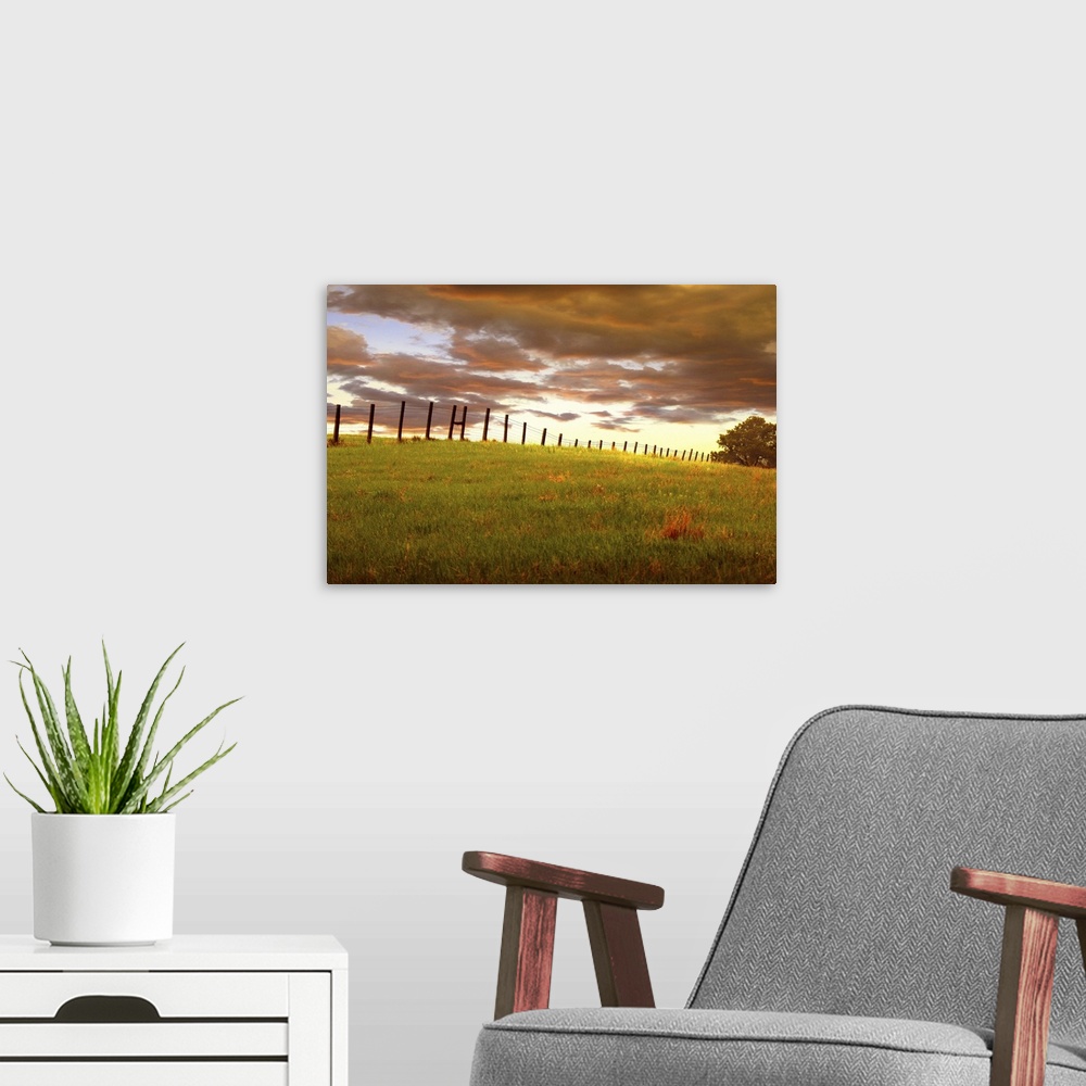 A modern room featuring Sunset with dramatic clouds over a fenced field, near Custer State Park, South Dakota.