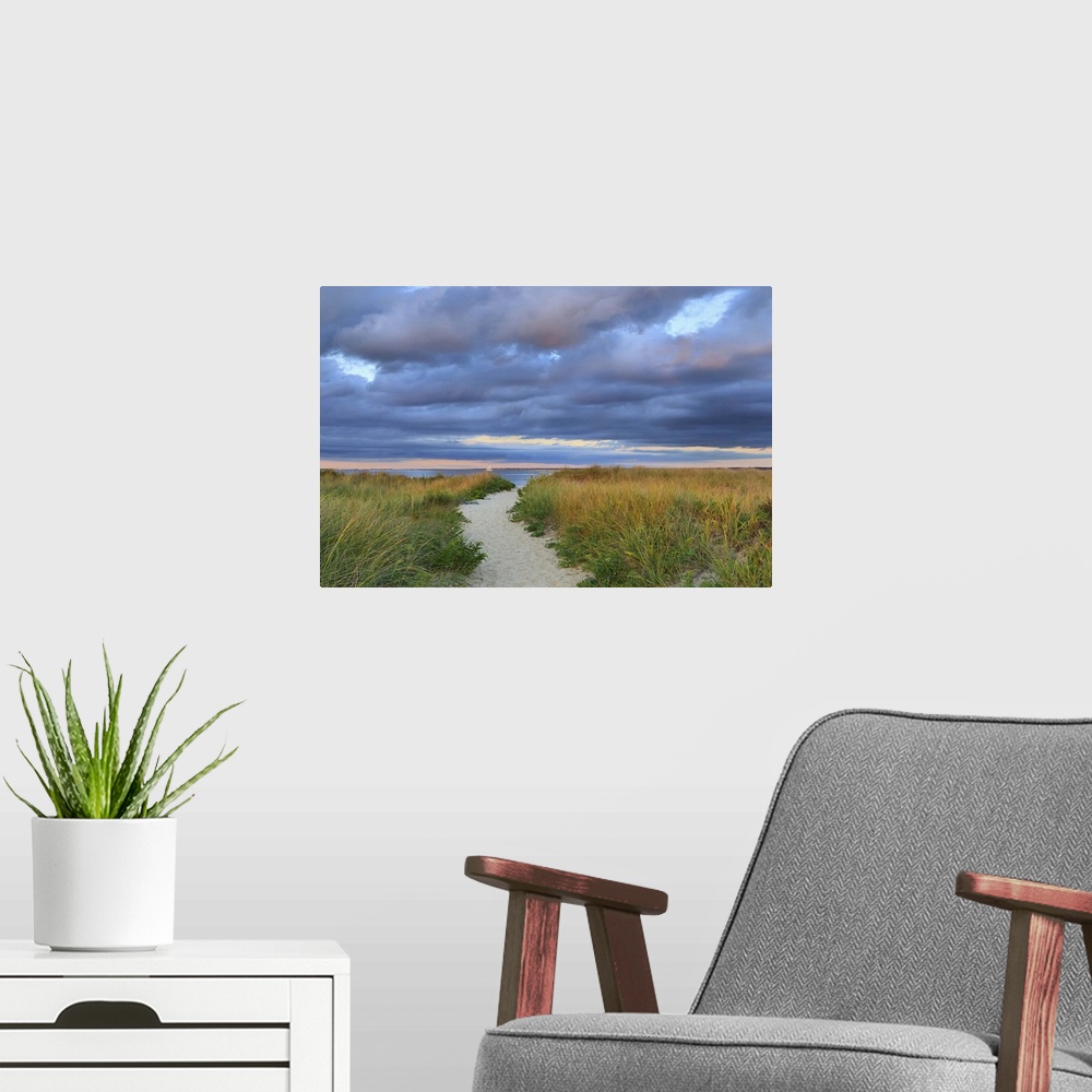 A modern room featuring A photograph of a sandy pathway leading to an idyllic beach, with dark puffy clouds overhead.