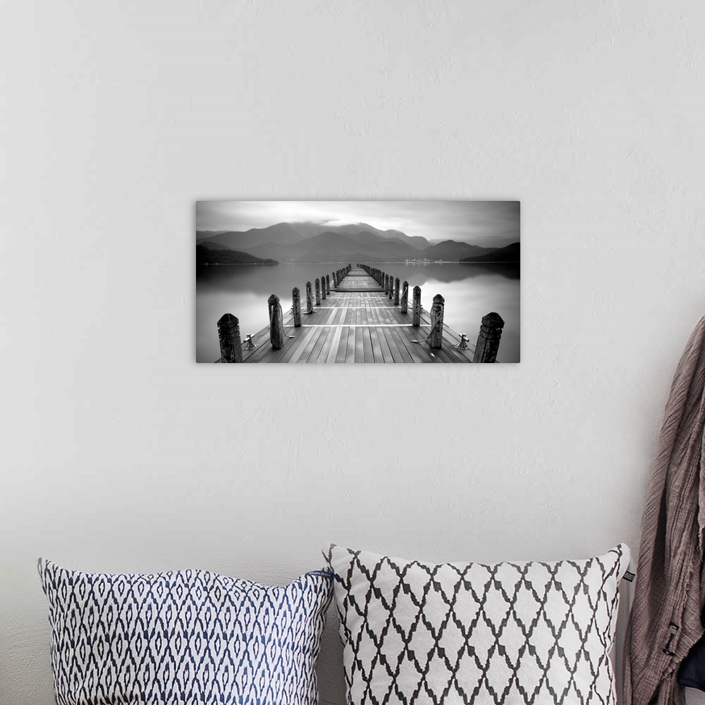 A bohemian room featuring A black and white photograph of a long pier at a lake with large mountains in the distance.