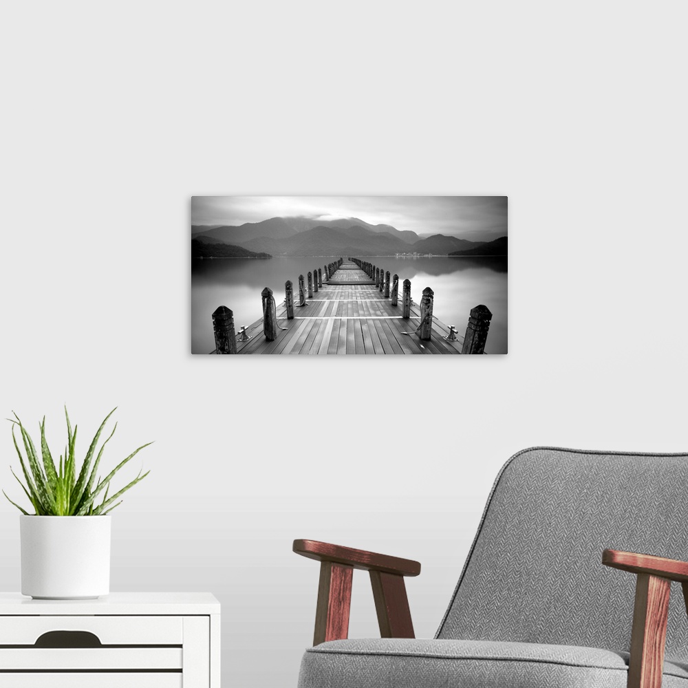 A modern room featuring A black and white photograph of a long pier at a lake with large mountains in the distance.