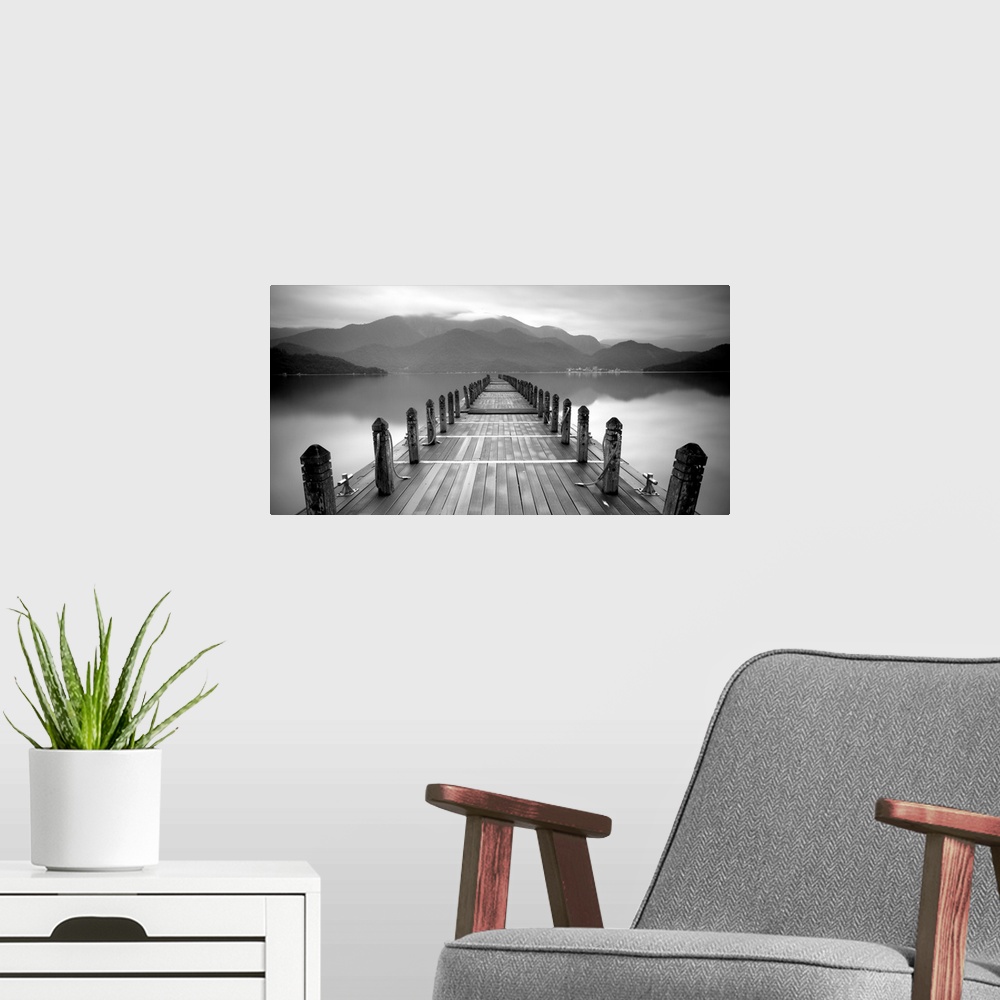 A modern room featuring A black and white photograph of a long pier at a lake with large mountains in the distance.
