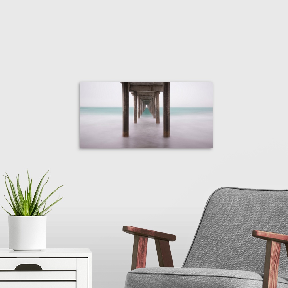 A modern room featuring A contemporary painting of the bottom side of a pier at a beach.
