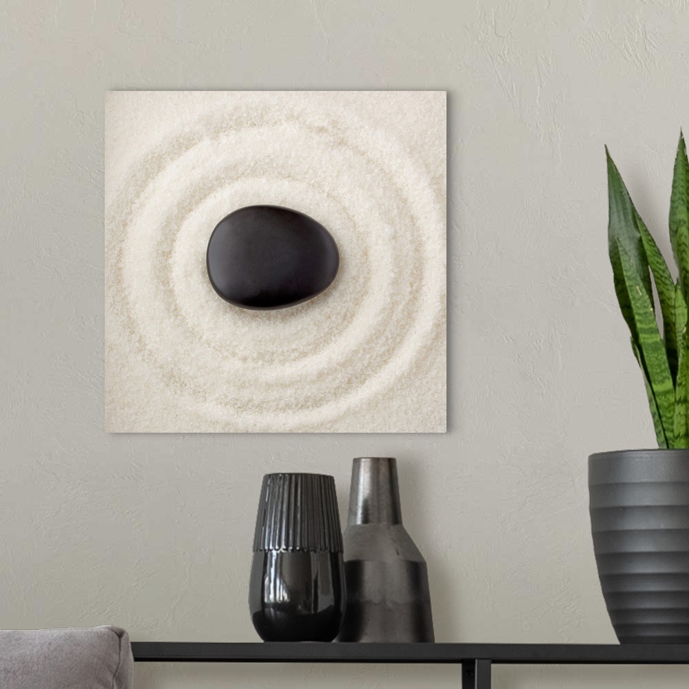 A modern room featuring A smooth black rock in the middle of multiple rings in the sand.