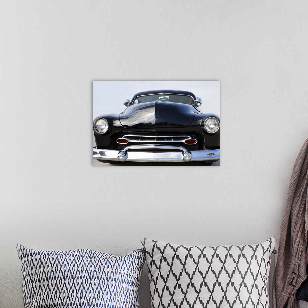 A bohemian room featuring The front of a classic car with a chrome bumper and dark paint.