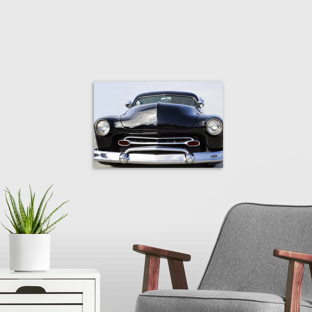 A modern room featuring The front of a classic car with a chrome bumper and dark paint.