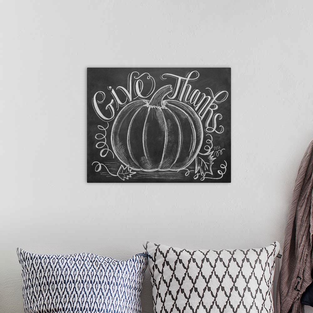 A bohemian room featuring "Give Thanks" handwritten with a drawing of a large pumpkin in white chalk on a black background.