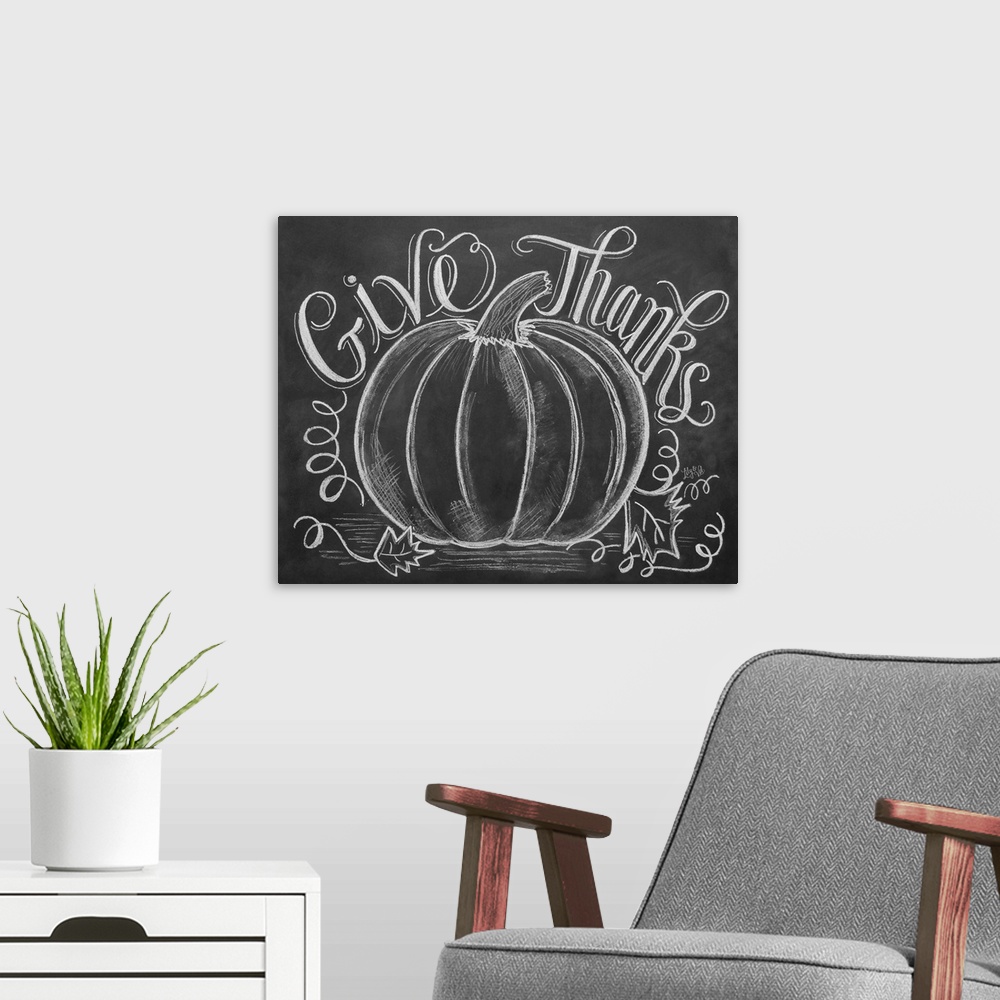 A modern room featuring "Give Thanks" handwritten with a drawing of a large pumpkin in white chalk on a black background.